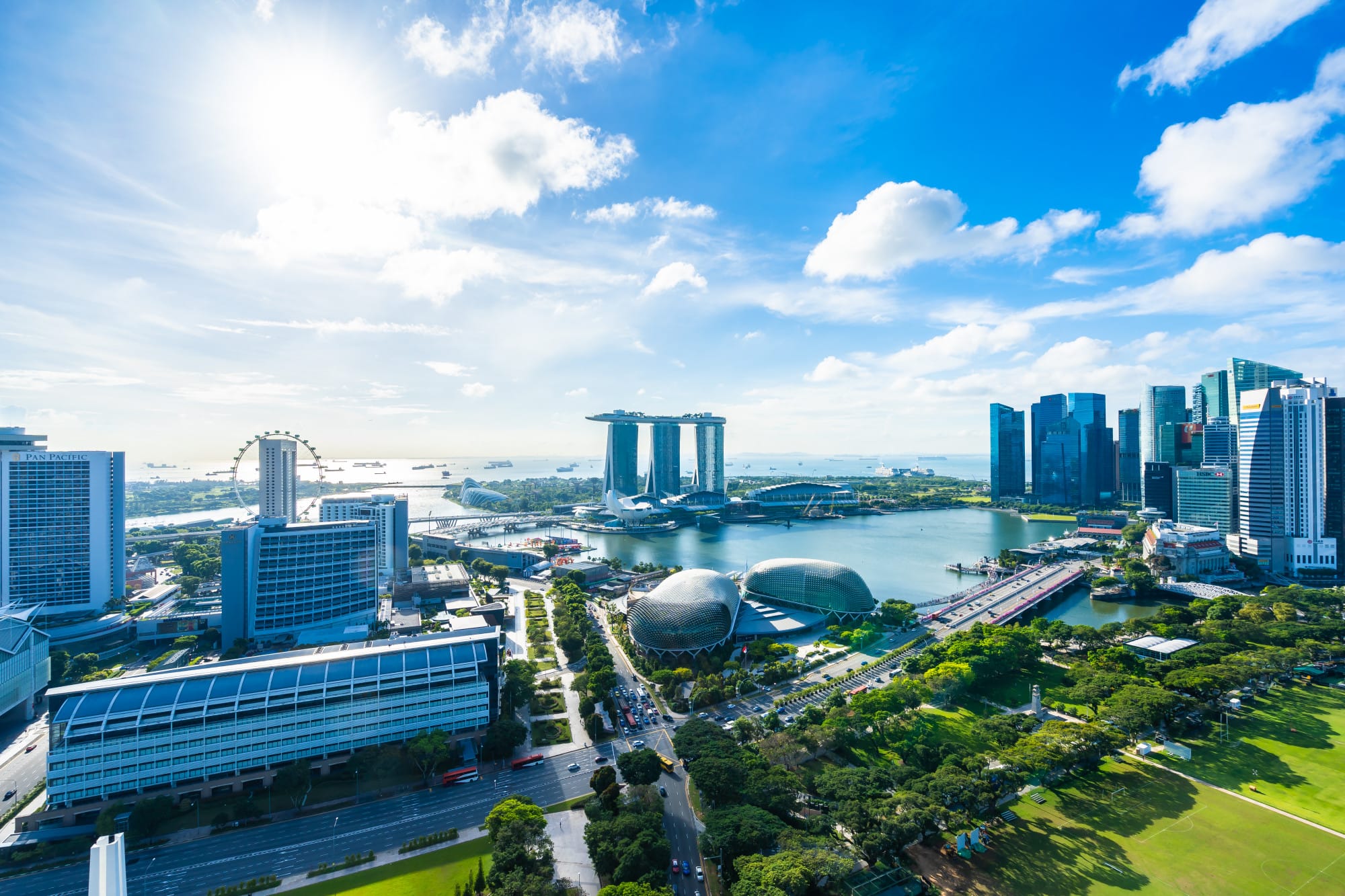 Aerial view of Singapore's Marina Bay with the three-tower hotel, Ferris wheel, dome theaters, and city skyline.